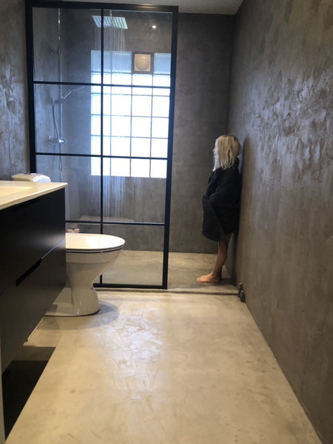 Badrum i Gråbeige microcement – dusch, toalett, badrock, person