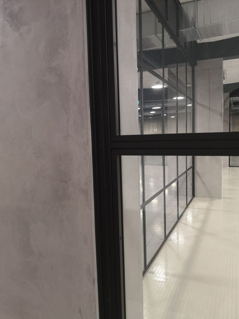Vägg i mörkgrå microcement – glasparti, svarta detaljer, ram